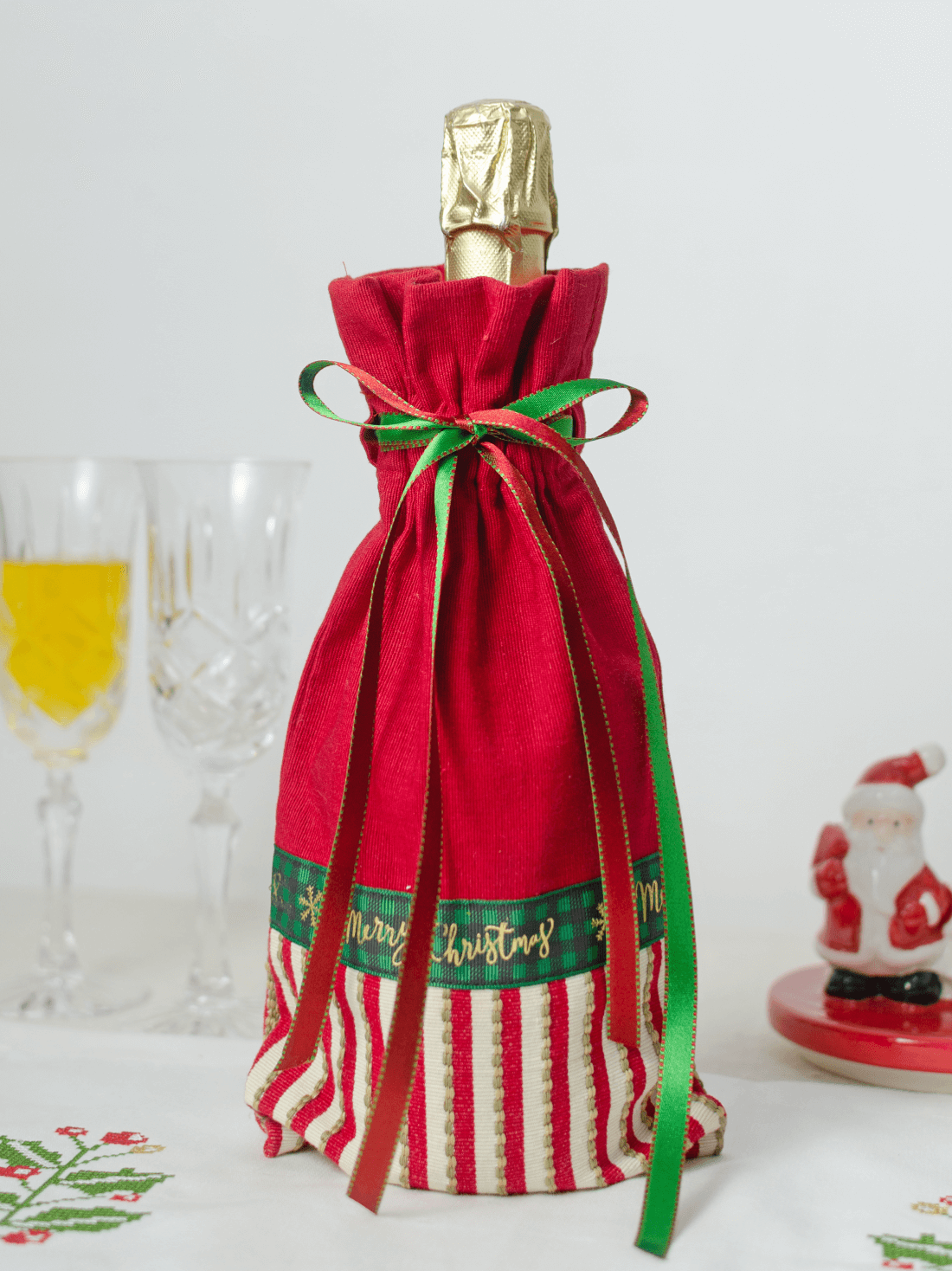 Bottle wrapped in a red Christmas gift bag with striped Merry Christmas trim and a green ribbon