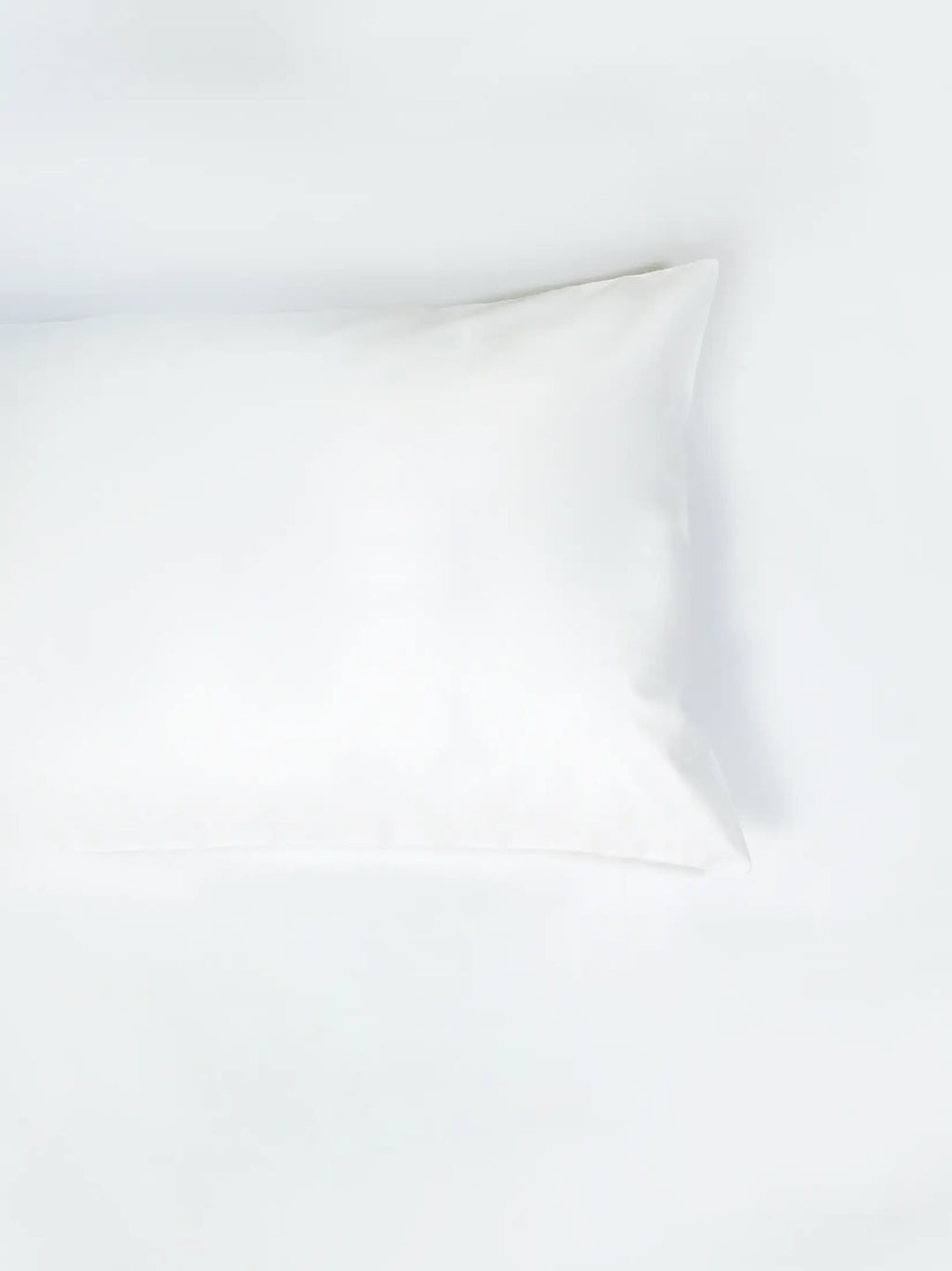 Plain white pillowcase resting on white bedding