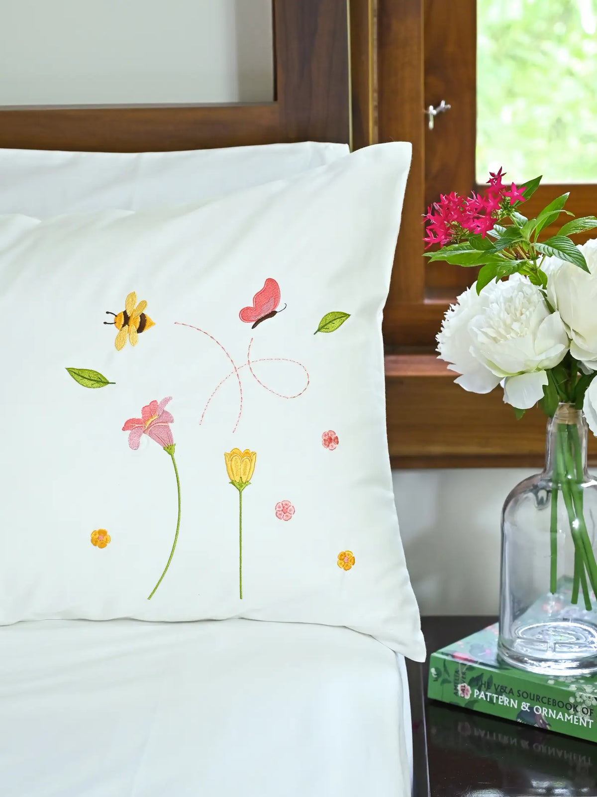 White pillowcase with embroidered bees, butterfly and pink and yellow flowers