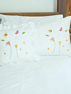 Two white Bees and Blossom embroidered pillowcases, one plain edged and one ruffled