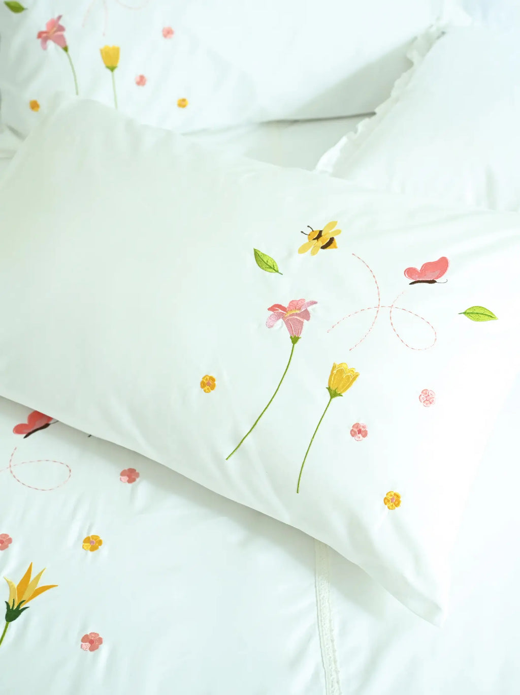 Close-up of white bed linen with bee, butterfly and floral embroidery