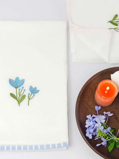 White Kerala bath towel with blue floral embroidery and a blue striped border beside a candle