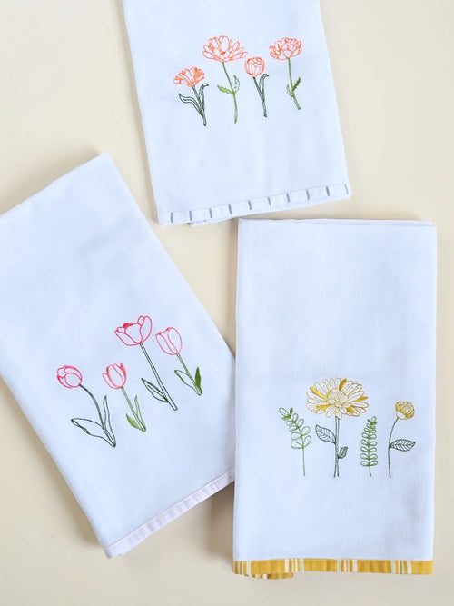Three white Kerala bath towels with pink, orange and yellow floral embroidery and coloured border trims