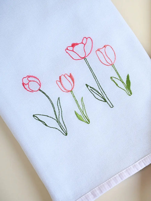 Close-up of pink tulip embroidery and pale pink border trim on a white Kerala bath towel