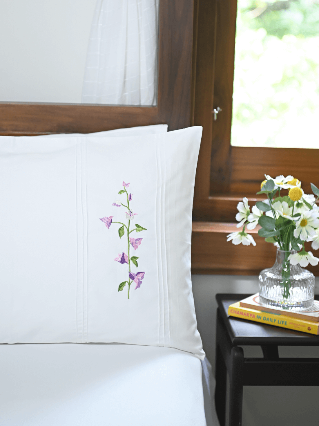 White pillowcase with pink and purple bougainvillea embroidery beside a vase of flowers