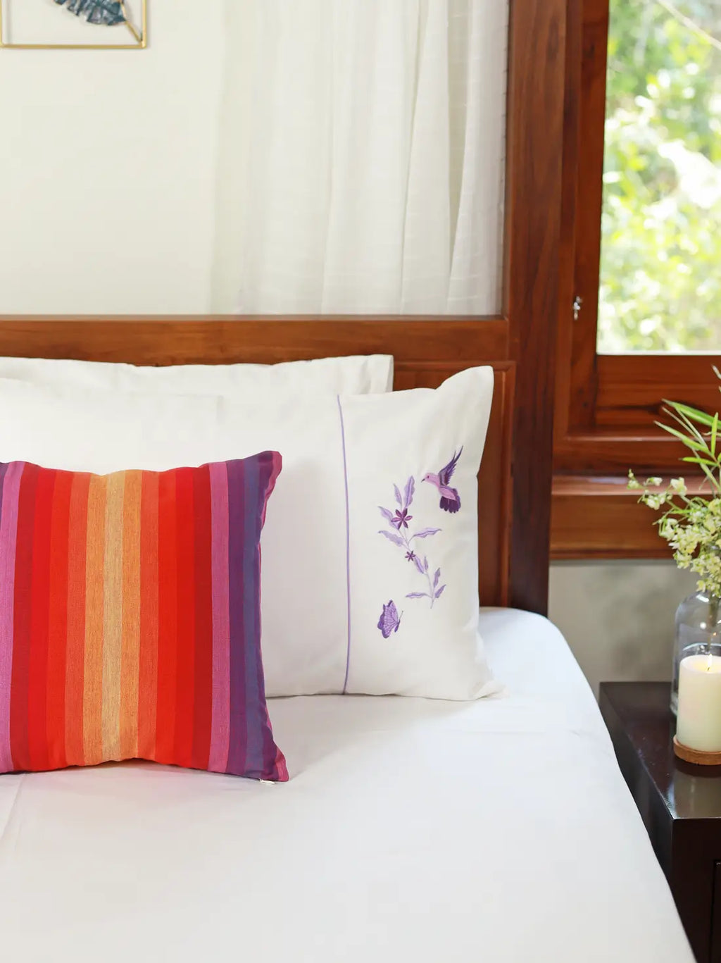 Red, orange and purple striped cushion cover on a white bed beside an embroidered pillow