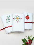 Three folded white towels embroidered with Christmas berries, a star snowflake and a red ornament