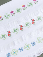 Three white Kerala bath towels with colourful floral and geometric cross-stitch embroidery and ruffled edges