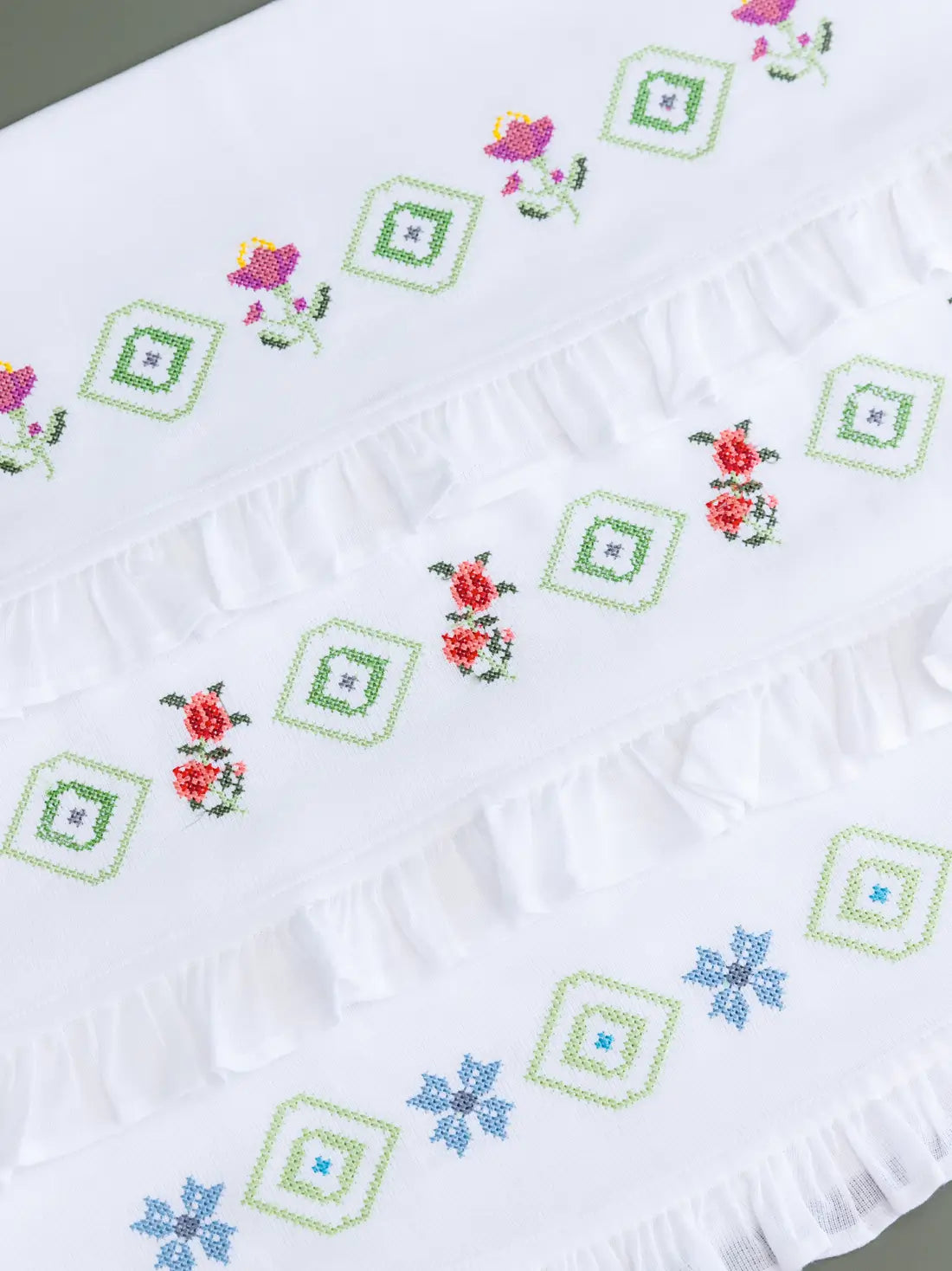 Three white Kerala bath towels with colourful floral and geometric cross-stitch embroidery and ruffled edges