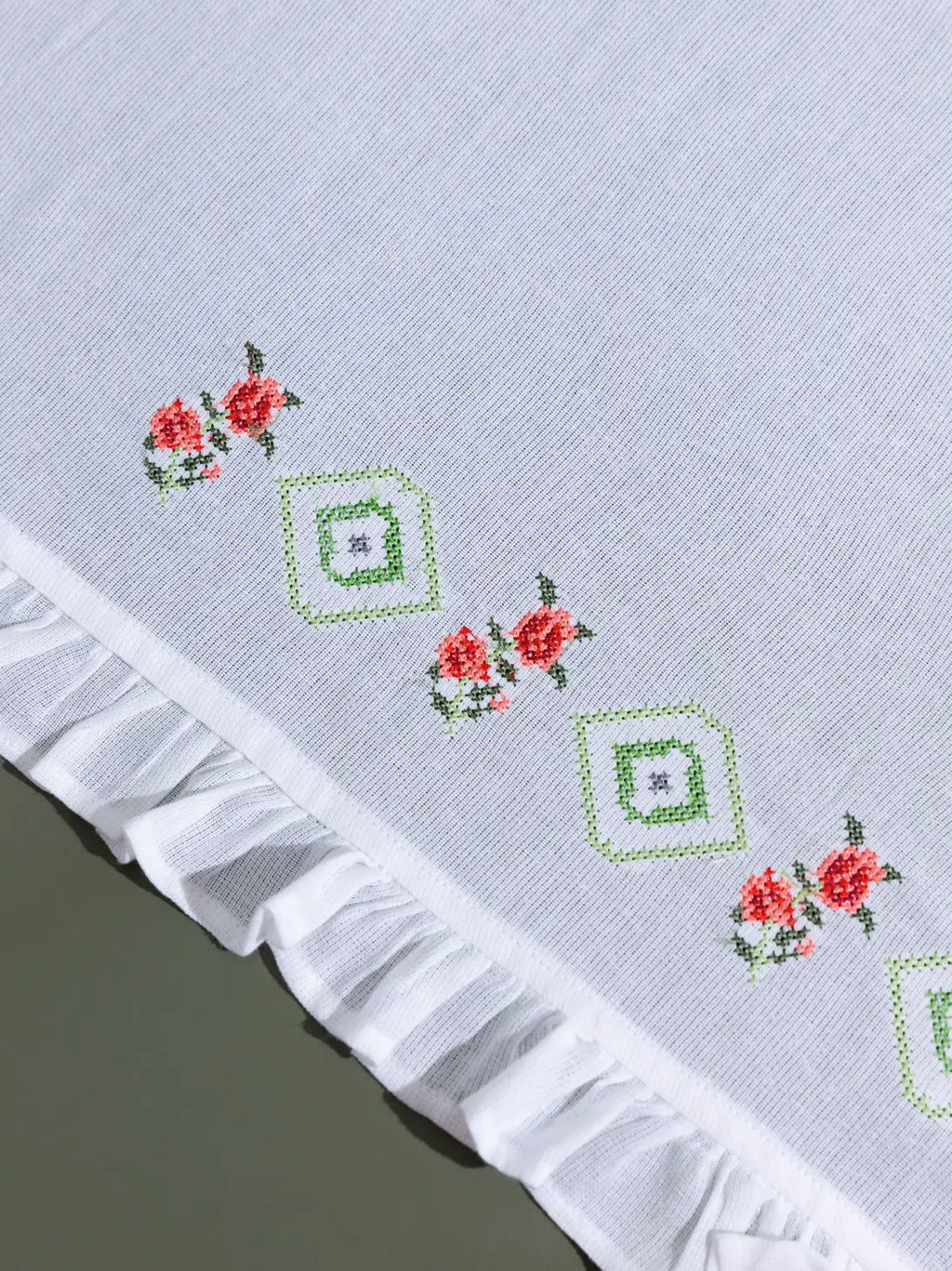Close-up of red floral and green geometric cross-stitch embroidery on a white ruffled towel