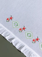 Close-up of red floral and green geometric cross-stitch embroidery on a white ruffled towel