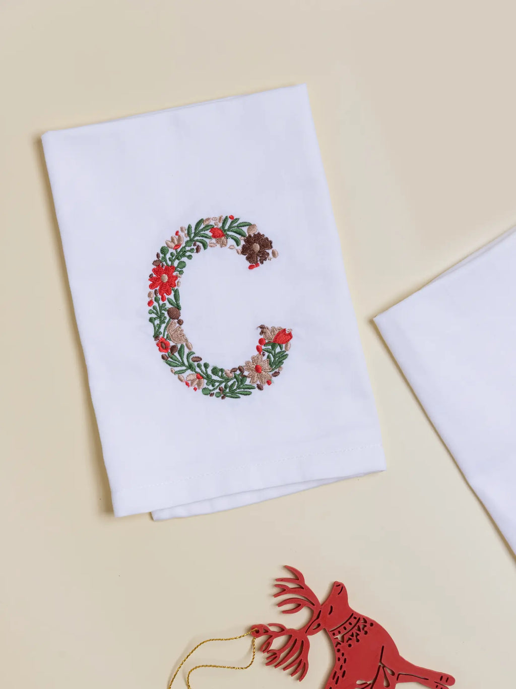 White napkin embroidered with a floral letter C in red, brown and green