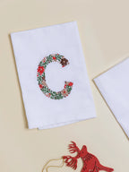 White napkin embroidered with a floral letter C in red, brown and green