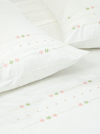 White bed sheet and pillowcases with pink and green floral embroidery, lace bands and dotted details