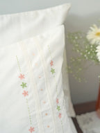 Close-up of a white pillowcase with pink and green floral embroidery, lace bands and pink dots