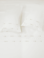 White bed sheet set with two pillowcases and rows of delicate floral embroidery