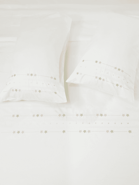 White bed sheet set with two pillowcases and rows of delicate floral embroidery