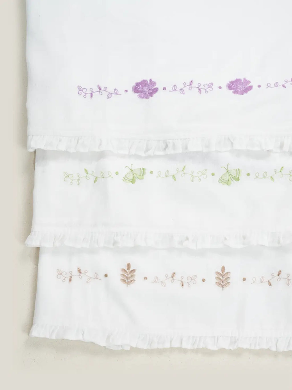 Three white Kerala Thorthu towels with purple, green and beige floral embroidery and ruffled edges