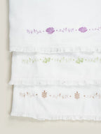 Three white Kerala Thorthu towels with purple, green and beige floral embroidery and ruffled edges