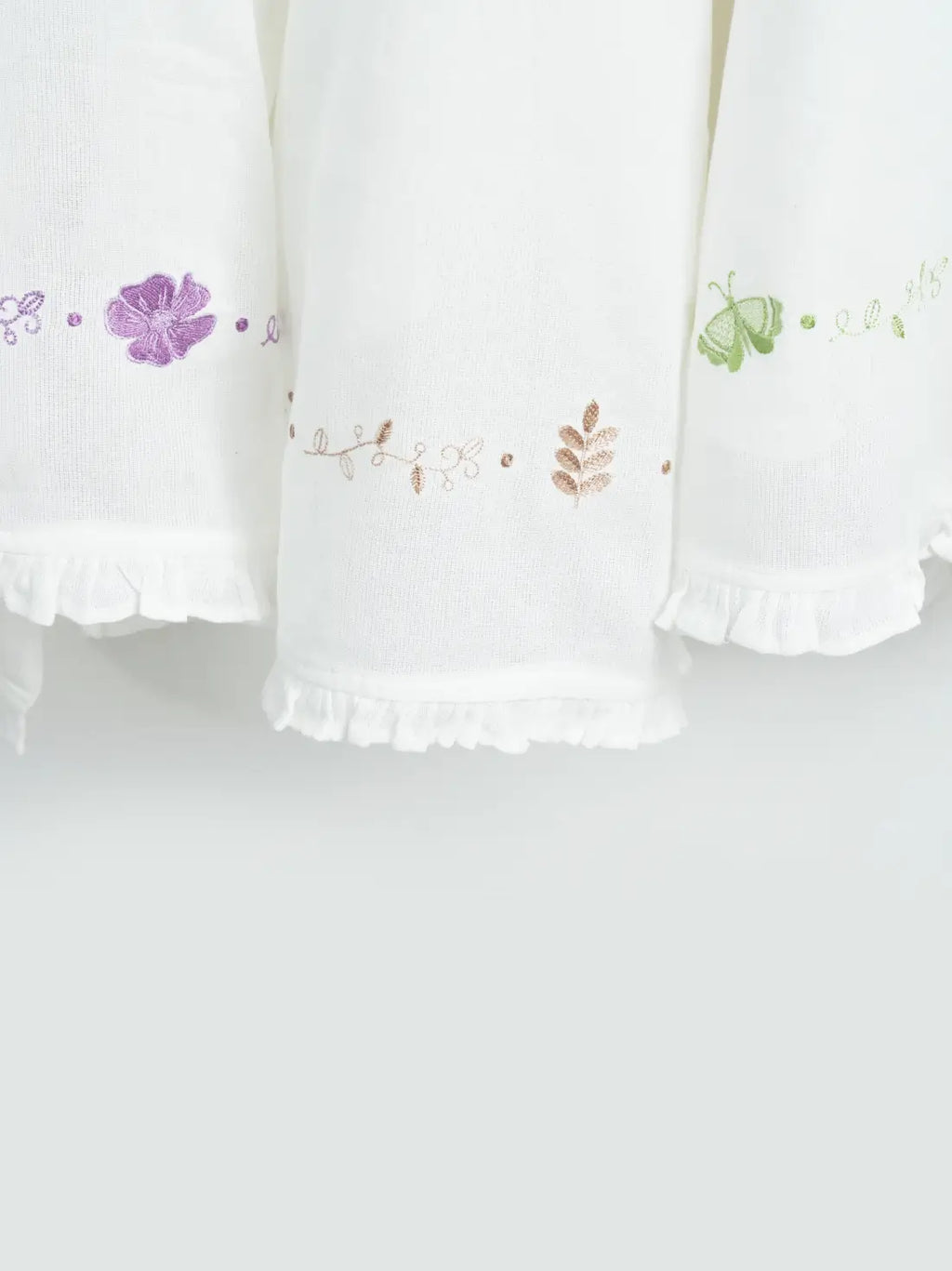 Close-up of three white Thorthu towels with floral embroidery and ruffled hems