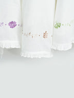 Close-up of three white Thorthu towels with floral embroidery and ruffled hems