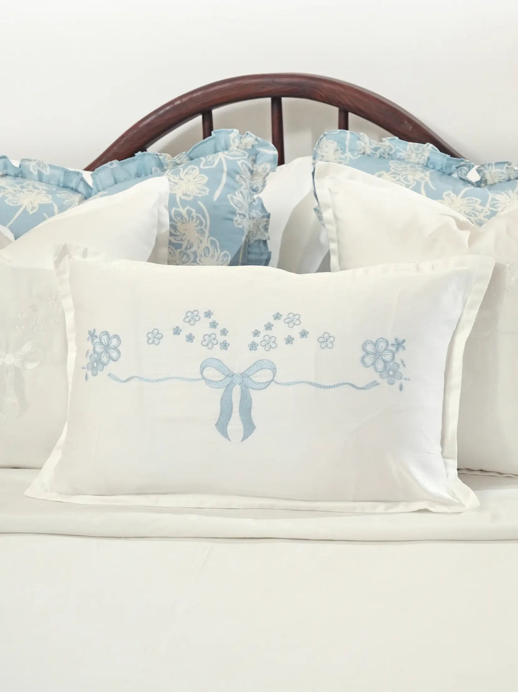 White cushion cover with a pale blue embroidered bow and small flowers styled on a bed