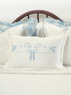 White cushion cover with a pale blue embroidered bow and small flowers styled on a bed