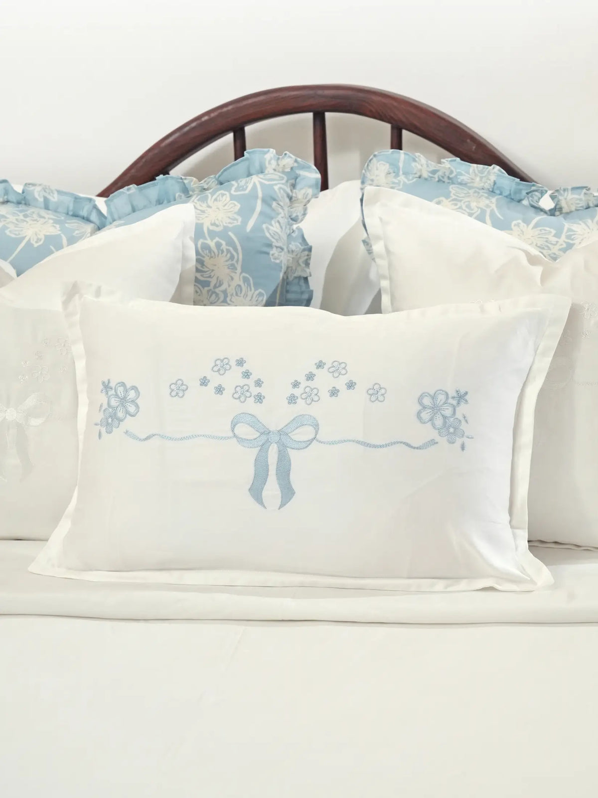 White cushion cover with a pale blue embroidered bow and small flowers styled on a bed