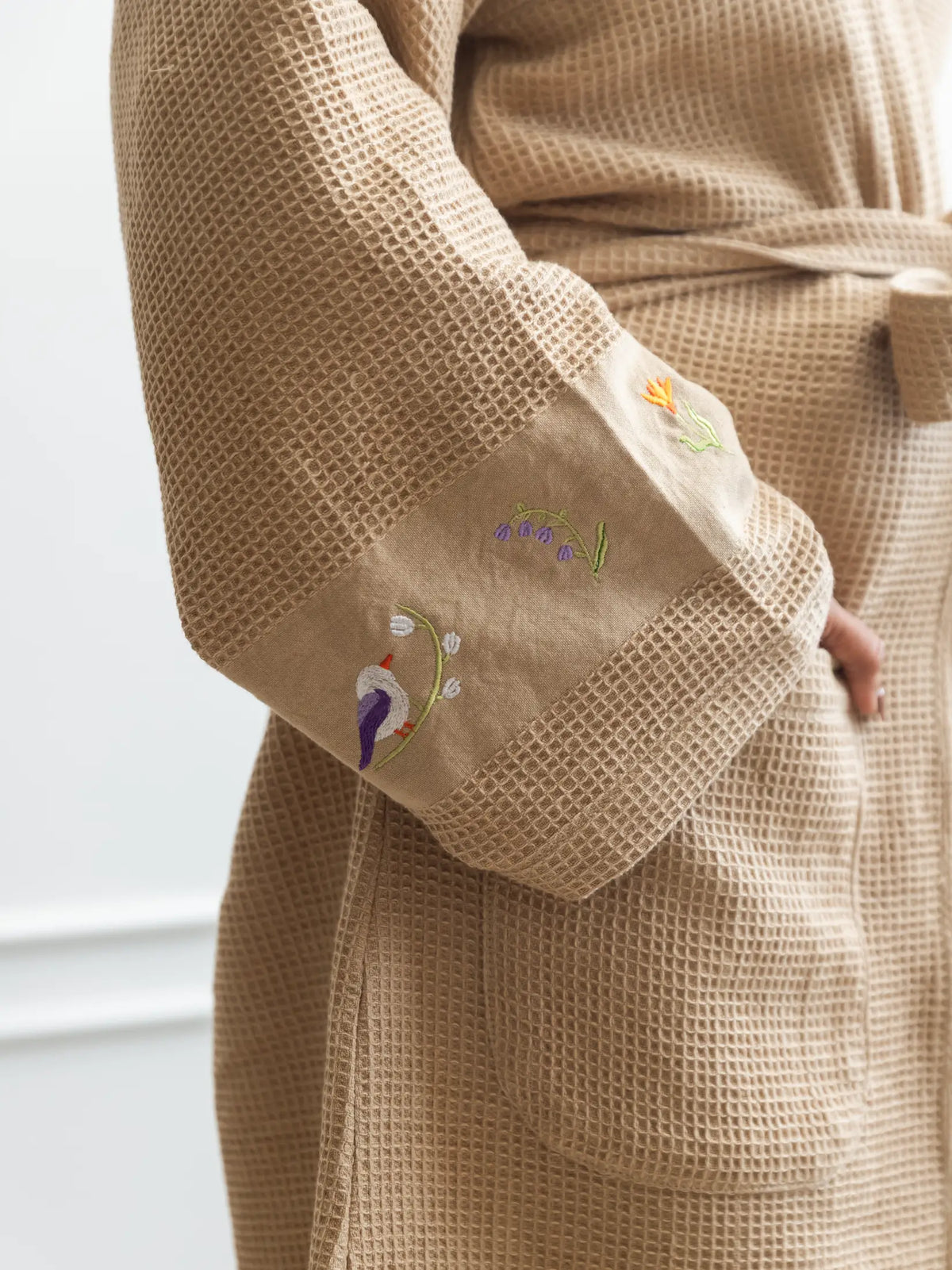 Close-up of bird and flower embroidery on the wide cuff of a beige waffle bath robe