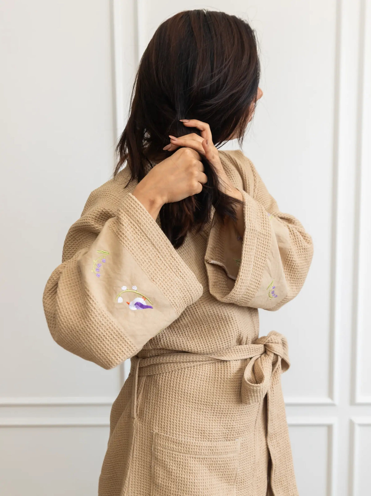 Woman wearing a belted beige waffle bath robe with embroidered wide sleeves and front pockets