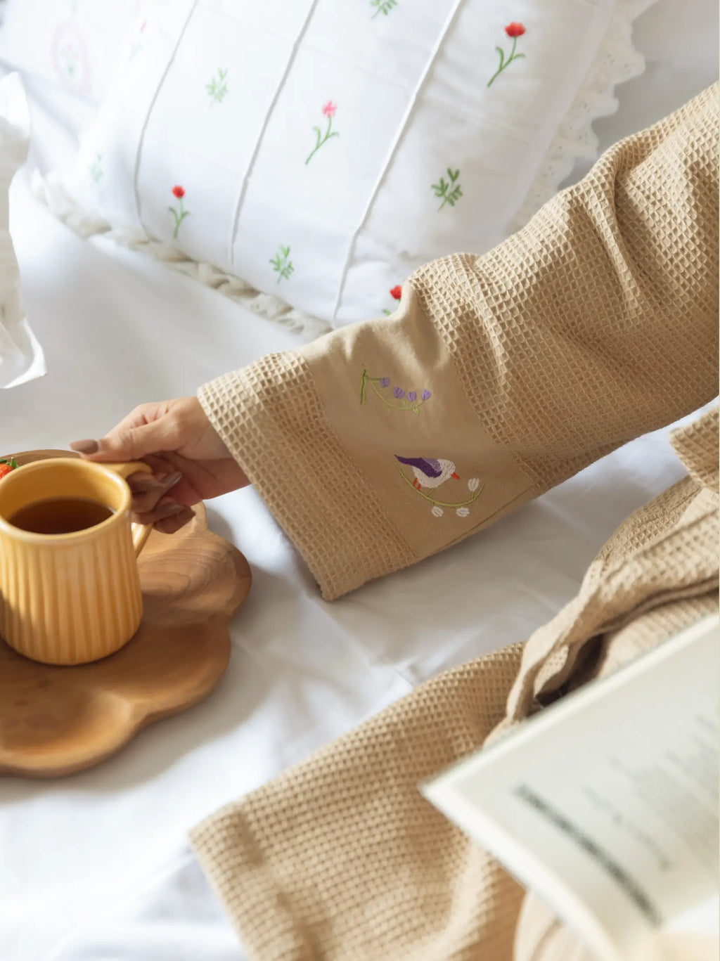 Embroidered cuff of a beige waffle bath robe beside a mug on a breakfast tray