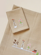 Folded cream honeycomb towels embroidered with potted plants, flowers, a bottle and books
