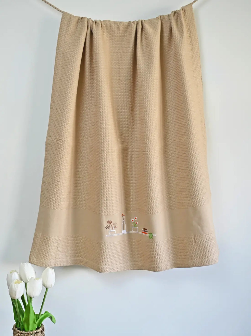 Cream honeycomb bath towel hanging with a garden shelf motif embroidered near the hem