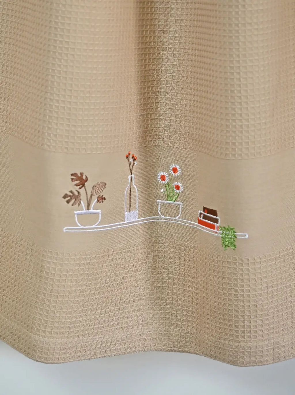 Close-up of potted plants, flowers, a bottle and books embroidered on a cream honeycomb towel