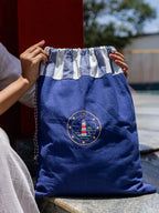 Woman holding a navy blue drawstring laundry bag with a grey and white striped top and lighthouse embroidery