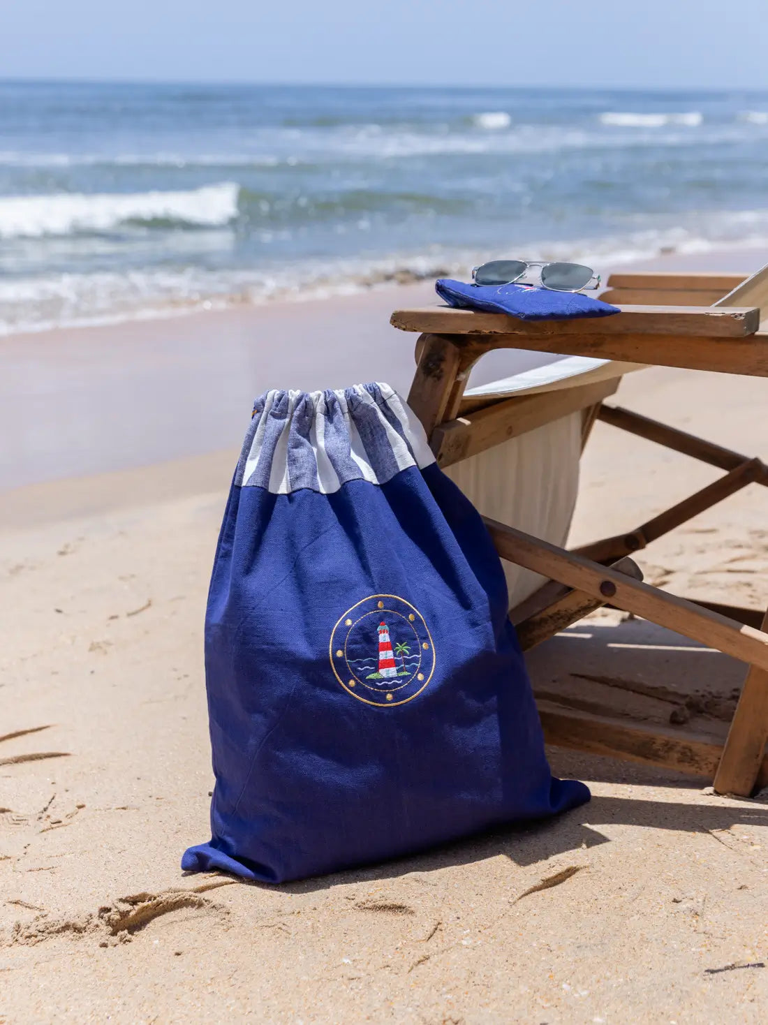 Navy blue lighthouse-embroidered drawstring laundry bag beside a beach chair