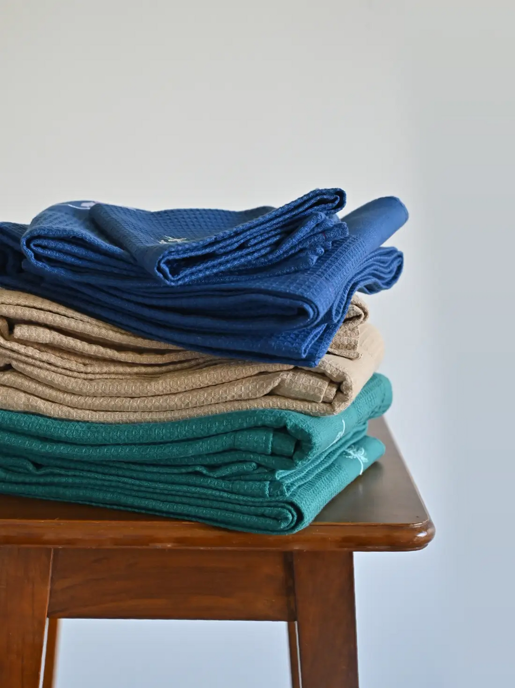Stacks of navy blue, cream and teal honeycomb towel sets on a wooden stool
