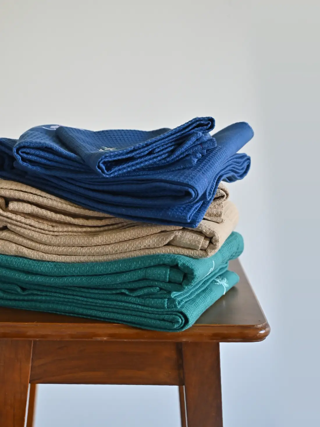 Stacks of navy blue, cream and teal honeycomb towel sets on a wooden stool