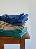 Stacks of navy blue, cream and teal honeycomb towel sets on a wooden stool