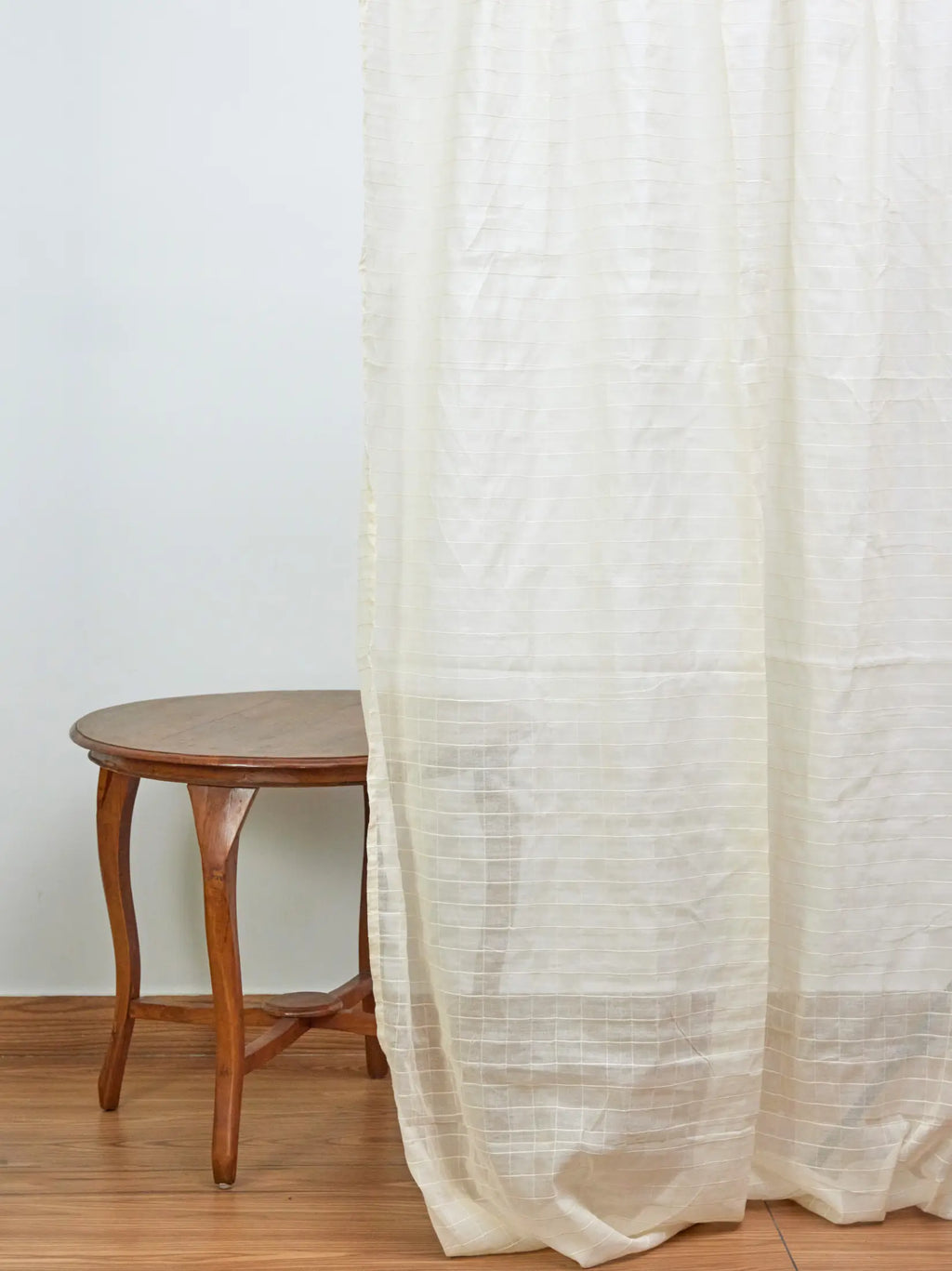 Full-length ivory cream sheer checked curtain beside a wooden stool