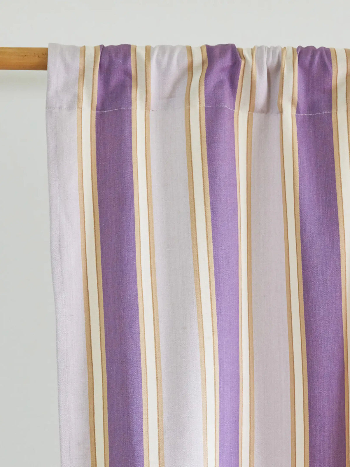 Close-up of a lavender, white and beige striped curtain gathered on a wooden rod