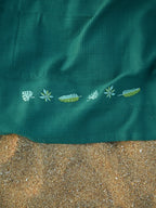 Close-up of tropical leaf embroidery on a teal green honeycomb towel on the sand