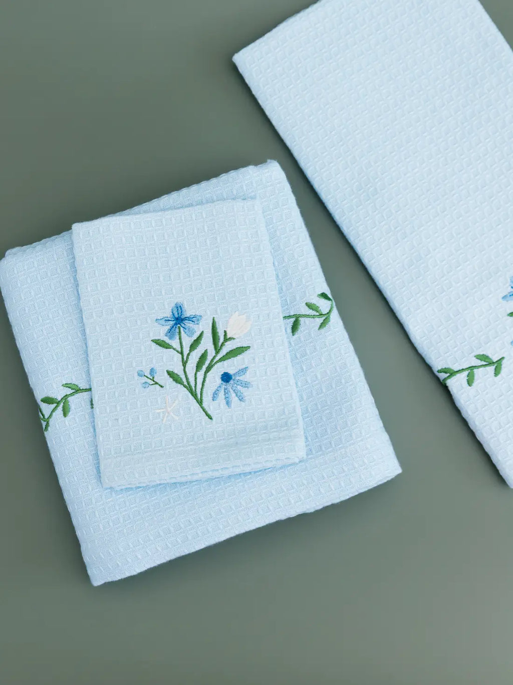 Three folded pale blue waffle towels with blue flowers and green vine embroidery