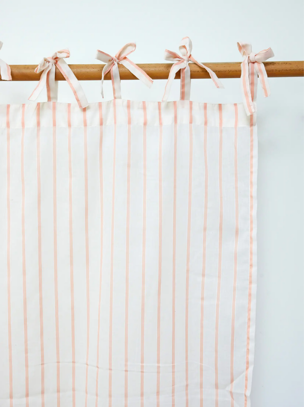 Peach striped sheer curtain panel with fabric ties on a wooden rod