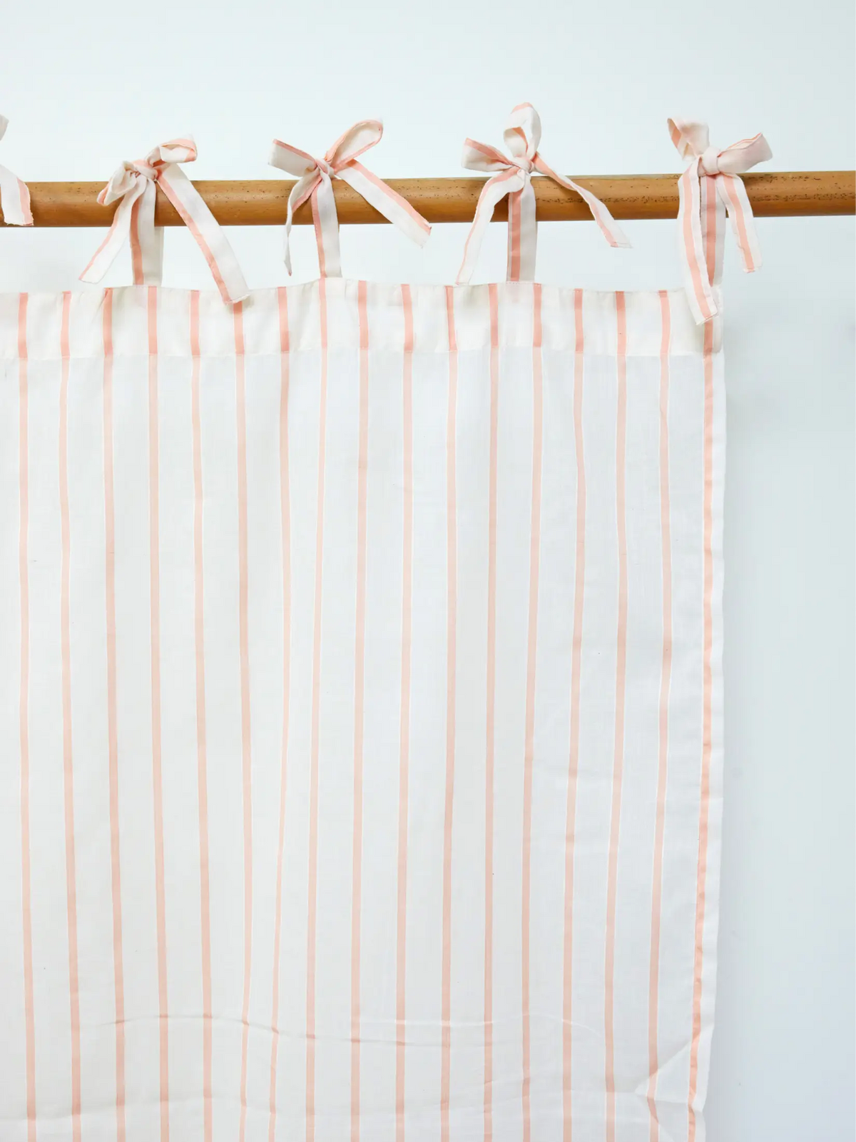 Peach striped sheer curtain panel with fabric ties on a wooden rod
