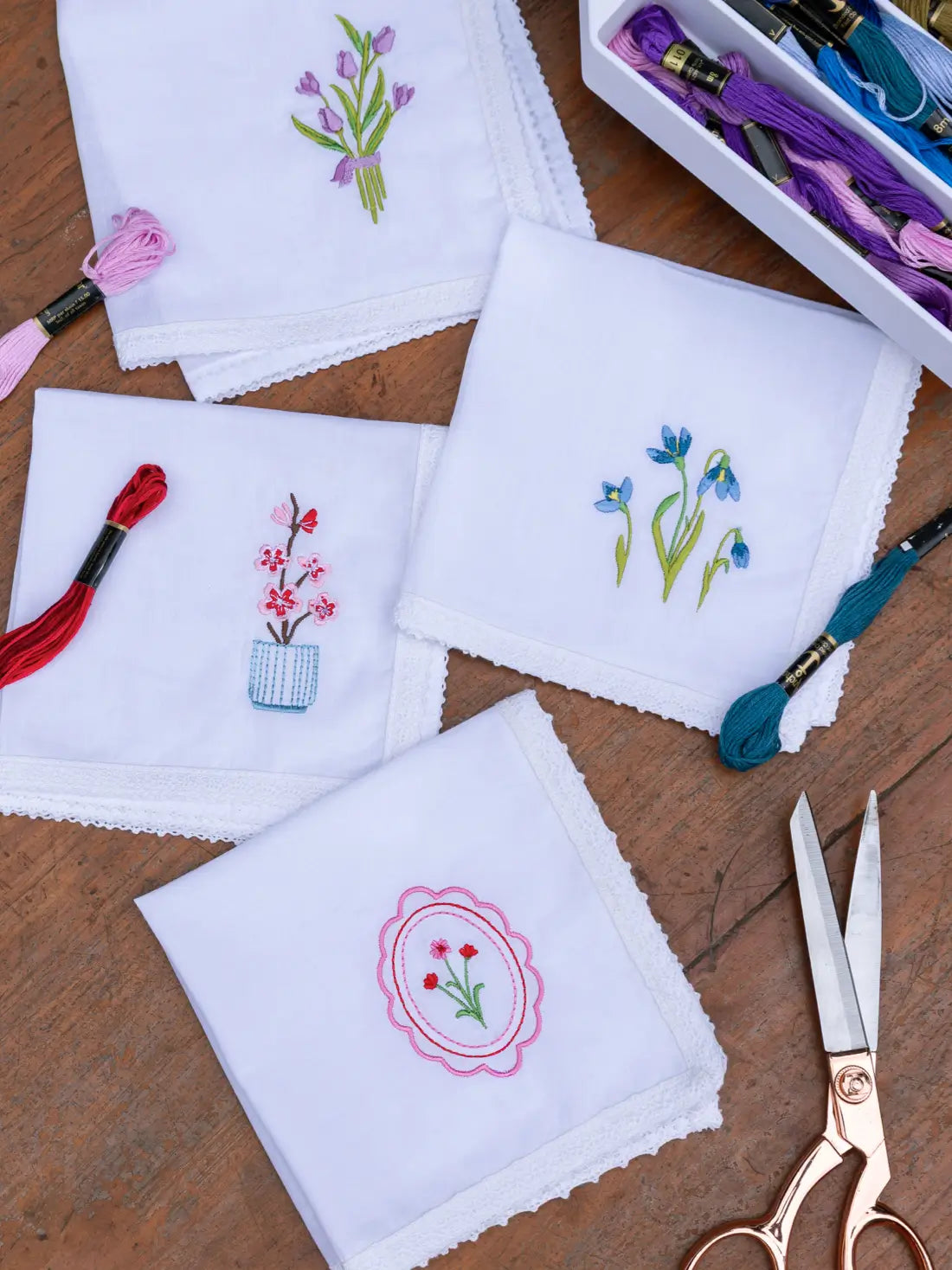 Four white embroidered handkerchiefs with floral motifs and lace edging