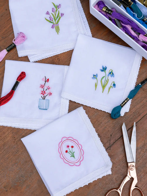 Four white embroidered handkerchiefs with floral motifs and lace edging