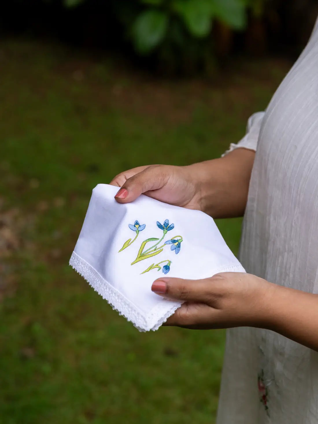 White handkerchief with blue floral embroidery and lace edge held outdoors