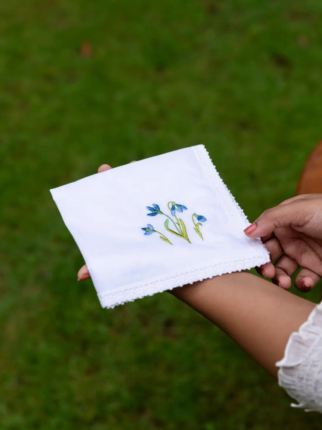 Folded white lace-edged handkerchief with blue floral embroidery