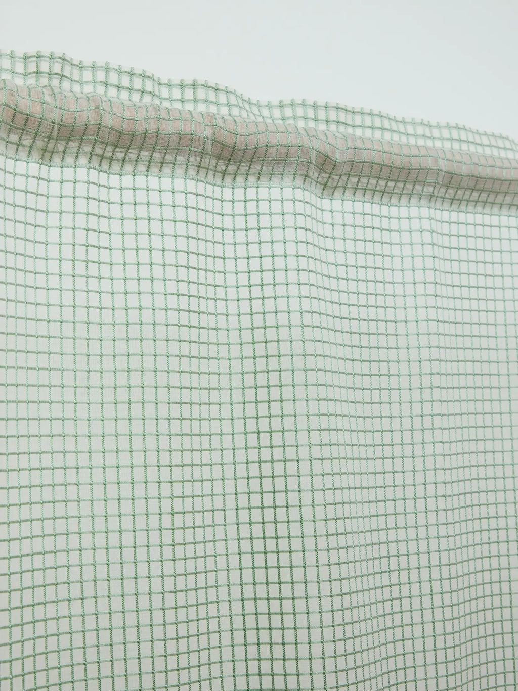 Close-up of the gathered rod pocket and green grid pattern on a white sheer curtain